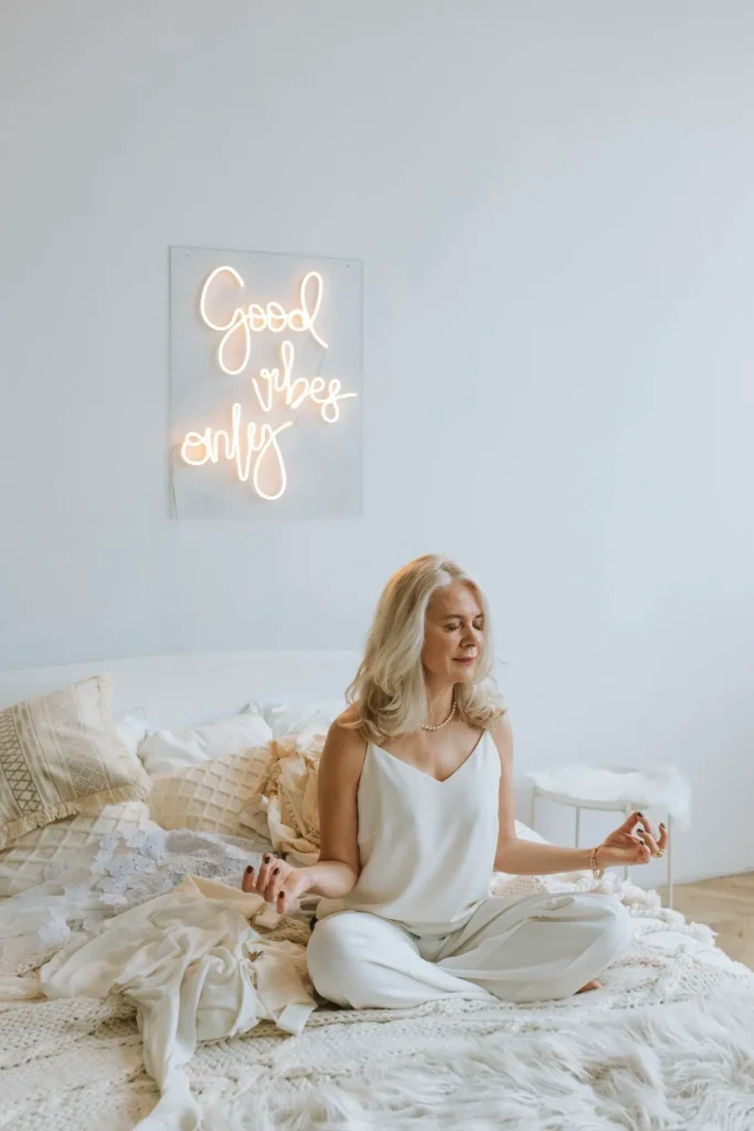 Frau sitzt mit geschlossenen Augen im Schneidersitz auf einem Bett