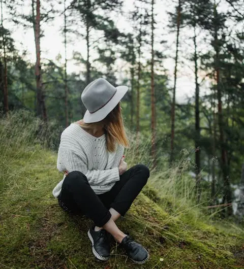 Frau mit Hut sitzt auf einem mit Moos bewachsenen Hügel im Wald